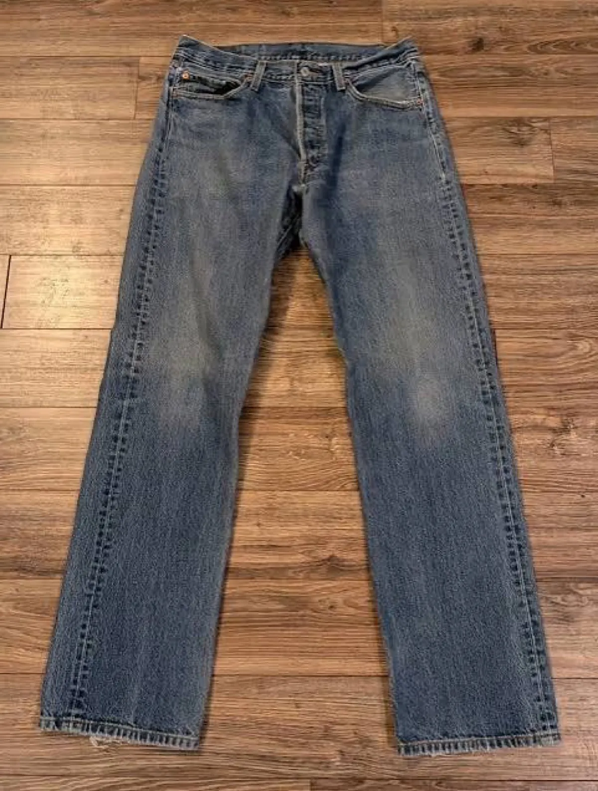 Vintage Levi's 501 jeans in medium wash laid flat on a hardwood floor
